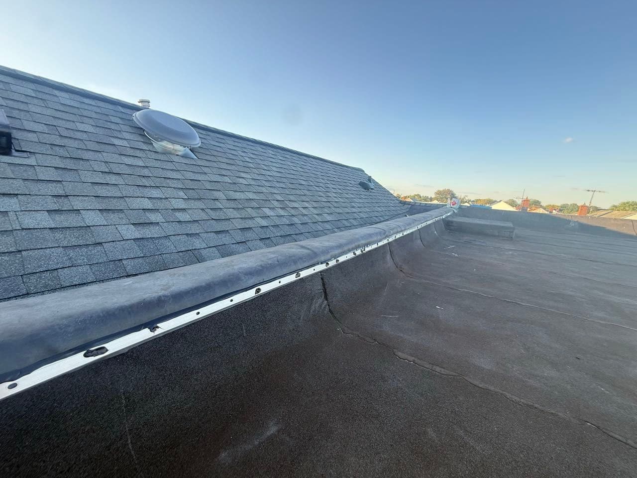 Transition where an asphalt shingle slope meets a black EPDM rubber flat roof on a Maryland home