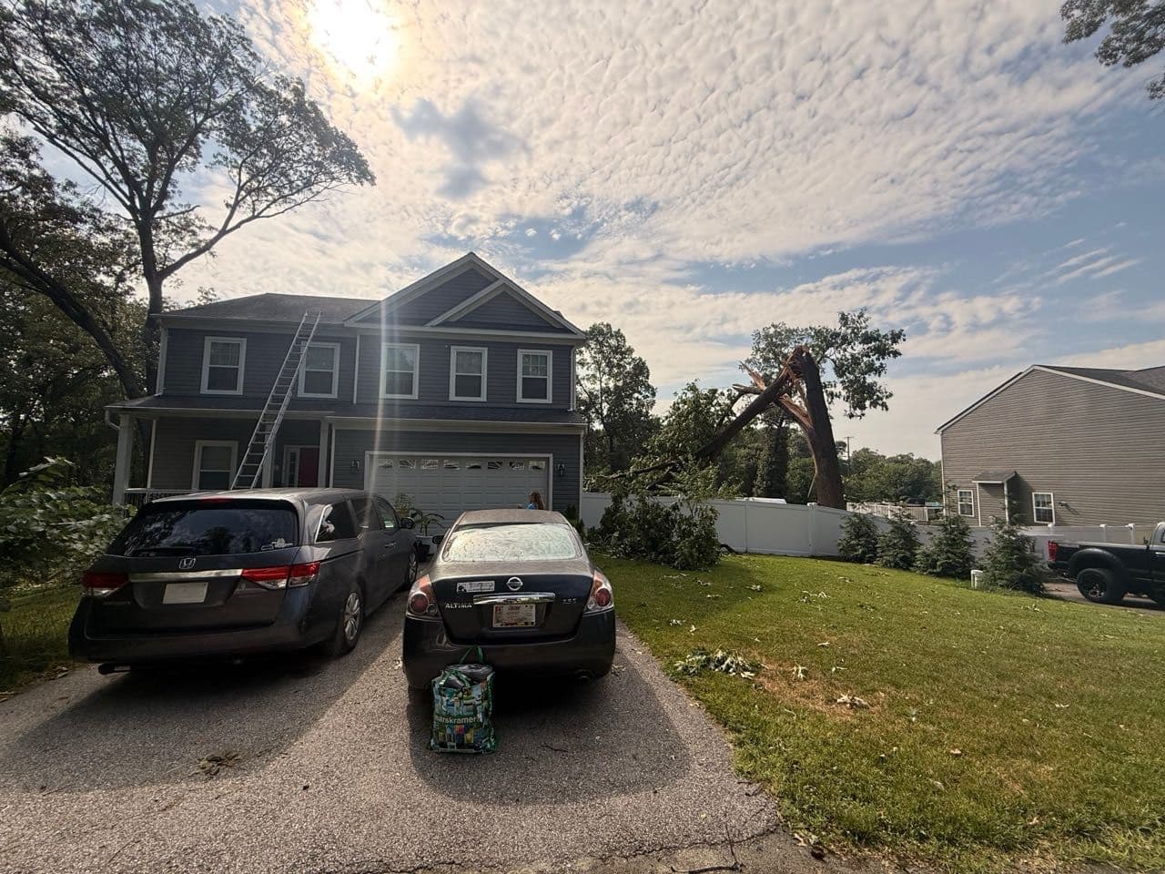 Storm-toppled tree beside a two-story Severn, Maryland home with an Apper Construction ladder set up for emergency roof inspection