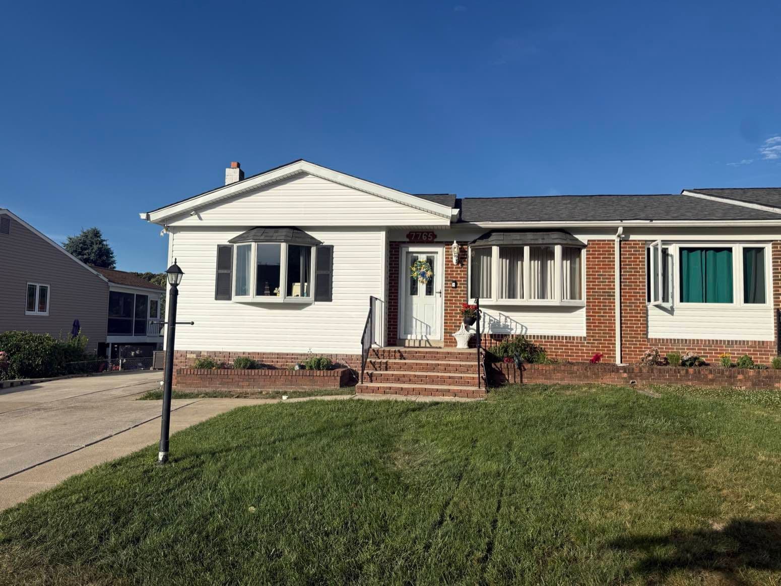Finished front elevation of a Pasadena, Maryland ranch home with new white CertainTeed Double 5-inch Dutchlap vinyl siding, black shutters, and brick accents after a full siding replacement